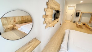 Une chambre d’hôtel avec une tête de lit en bois, un miroir rond, un téléviseur fixé au mur, un lit avec une literie blanche et une petite table de chevet en bois.