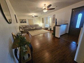 Un salon spacieux doté d’un plancher en bois, d’un ventilateur de plafond et d’une grande fenêtre.