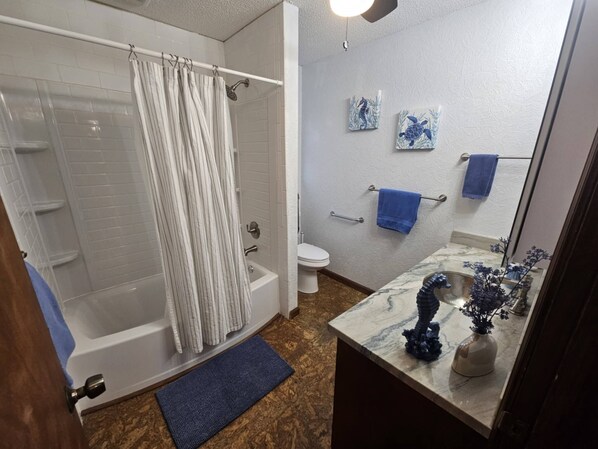 A bathroom with a bathtub, shower, toilet, and a marble countertop with a vase and decorative items. - Your Perfect Perdido Key Getaway (Pensacola)