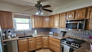 A kitchen with wooden cabinets, a stainless steel refrigerator, a microwave, a stove, and a ceiling fan. - Your Perfect Perdido Key Getaway (Pensacola)