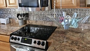 A kitchen with wooden cabinets, a stainless steel microwave, a stove, and a hanging utensil rack. - Your Perfect Perdido Key Getaway (Pensacola)