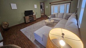 A living room with a sofa, ottoman, coffee table, and a television on a wooden cabinet. - Your Perfect Perdido Key Getaway (Pensacola)