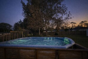Un bain à remous dans un jardin, avec une terrasse en bois et un arbre.