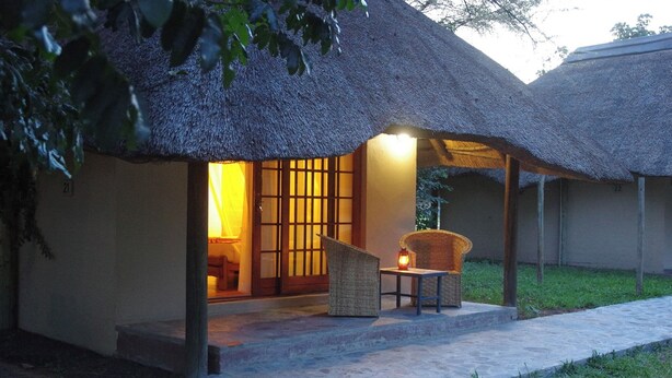 A thatched-roof structure with a stone-paved entrance and a wicker chair with a lantern. - Big 5 Toro Lodge (Kasane)