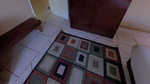A hallway with a tiled floor, a wooden door, and a patterned rug. - Big 5 Toro Lodge (Kasane)