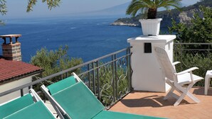 A terrace with green lounge chairs, a white table, and a potted plant. - The Phoenix White house (Massa Lubrense)