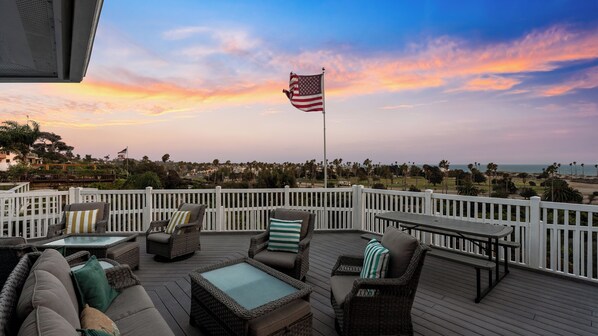 An outdoor deck with wicker furniture, a flag, and a view of the ocean.