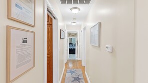 A hallway with framed documents on the walls, a wooden door, and a bed in the background.