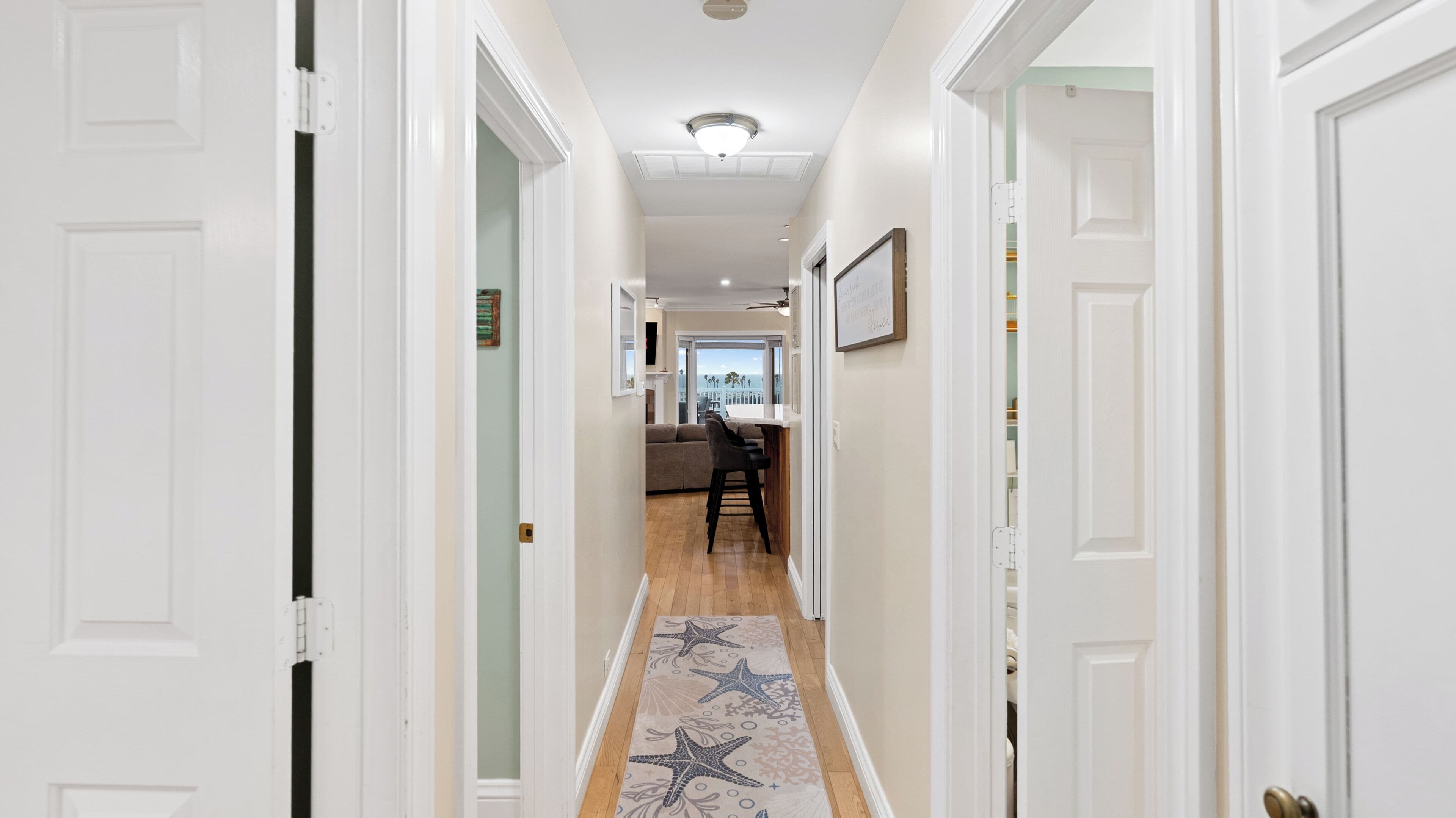 A hallway with white doors, a wooden floor, and a starfish-patterned rug.
