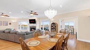 A spacious living room with a fireplace, a dining area with a wooden table and chairs, and a balcony with a view.