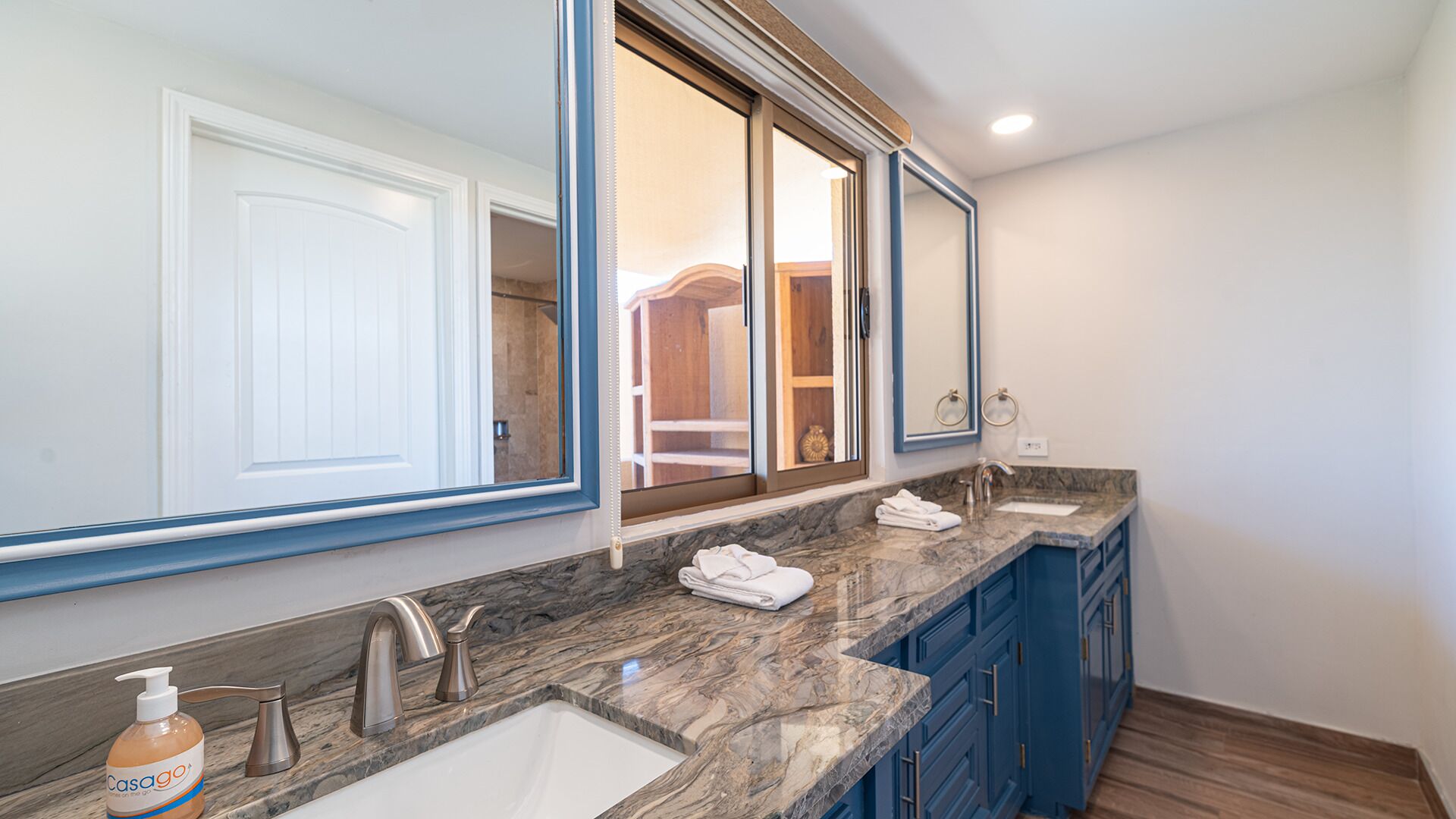 A modern bathroom with two sinks, a large mirror, and a walk-in shower visible through the glass door.
