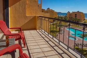 A balcony with red chairs, a tiled floor, and a view of a swimming pool and buildings. - Princesa De Penasco (Puerto Peñasco)