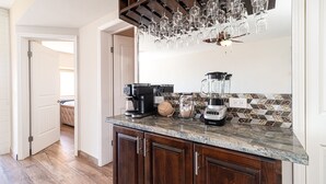 Eine Küche mit dunklen Holzschränken, einer Granitabdeckung, einer Kaffeemaschine, einem Mixer und einer Hängeleuchte mit Weingläsern.