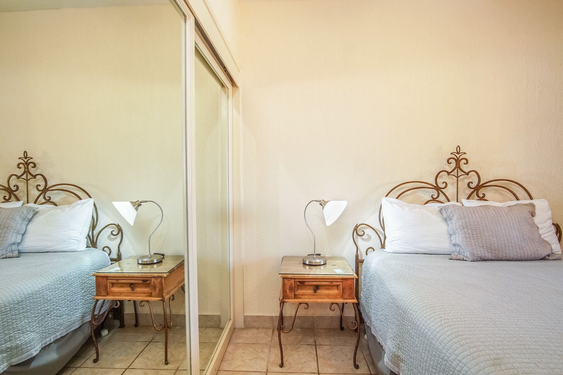 Une chambre à coucher avec deux lits, chacun doté d’une table de chevet et d’une lampe, d’un miroir et d’un sol carrelé.