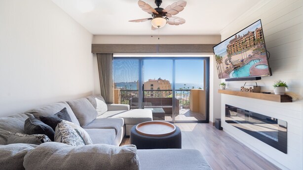 Ein modernes Wohnzimmer mit großem Fenster, Deckenventilator, Flachbildfernseher und Kamin.
