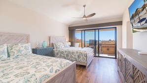 Ein Hotelzimmer mit zwei Betten, einem Deckenventilator, einem Balkon mit Blick und einem Gemälde an der Wand.