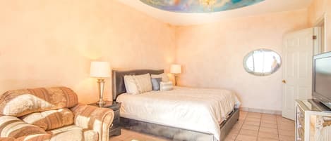 Een slaapkamer met een bed, twee nachtkastjes met lampen, een bank, een plafondschildering, een ronde spiegel en een televisie.