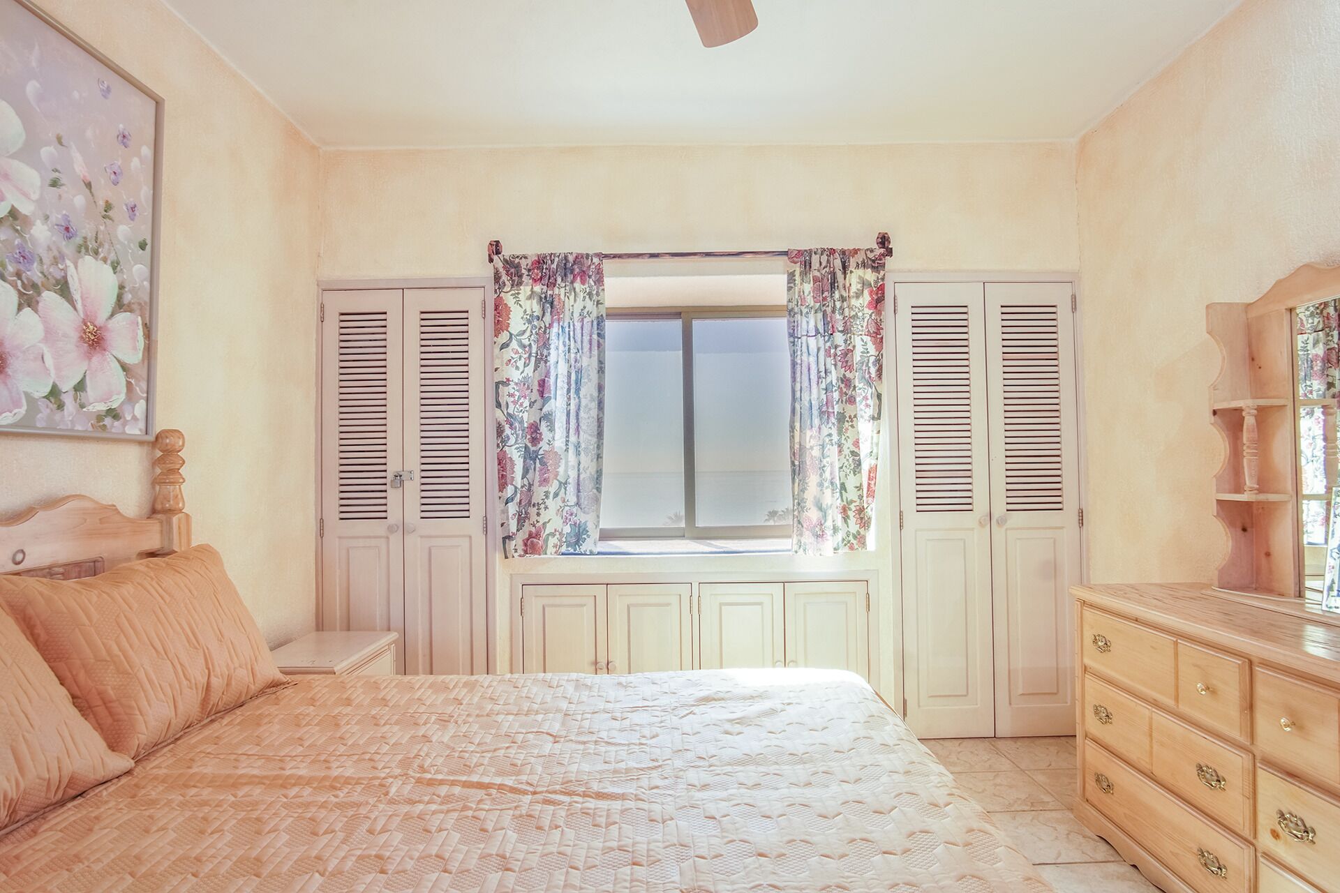 Un dormitorio con cama, cómoda y ventana con cortinas florales.