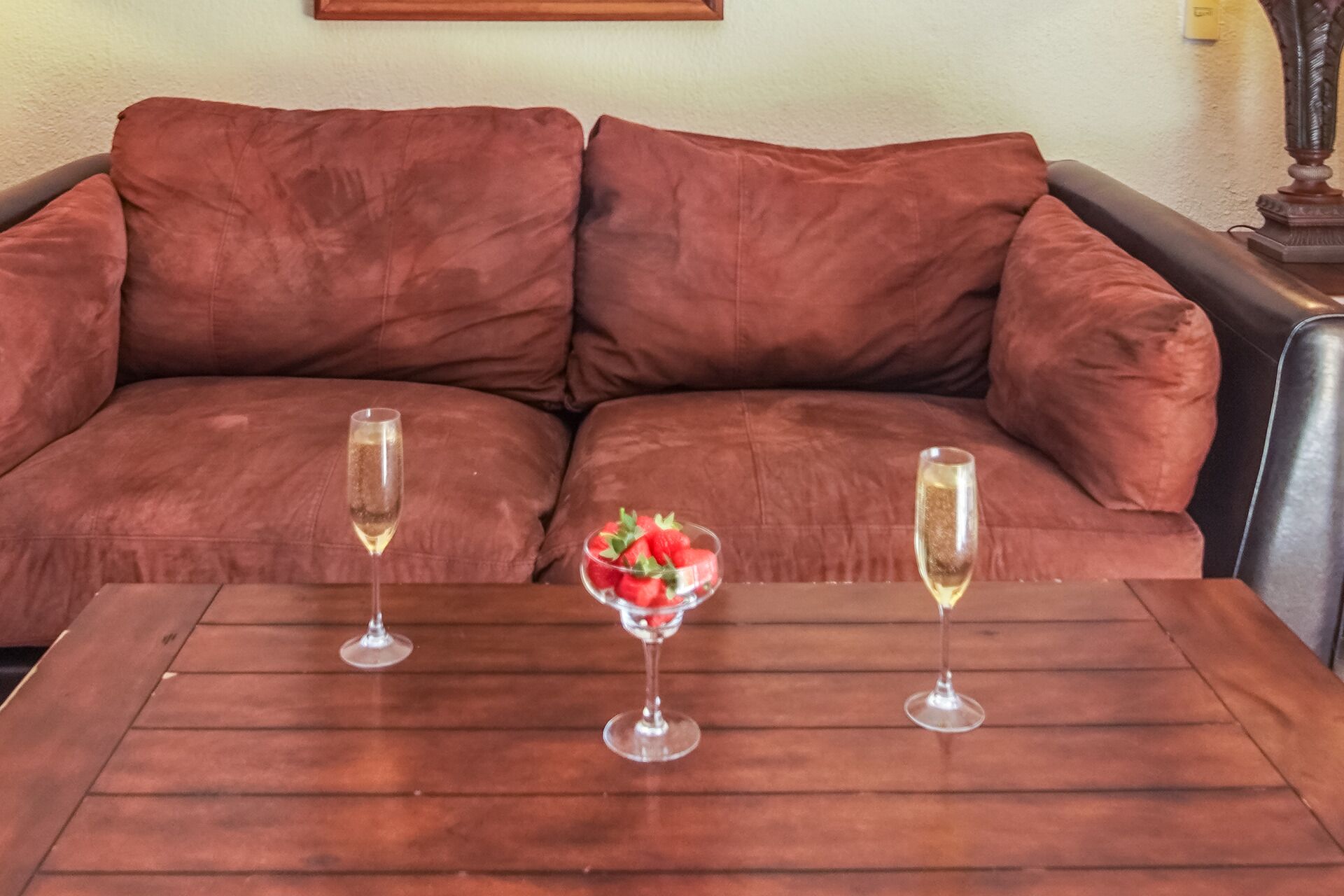 Ein braunes Sofa mit zwei Sektgläsern und einer Schale Erdbeeren auf einem Holztisch.