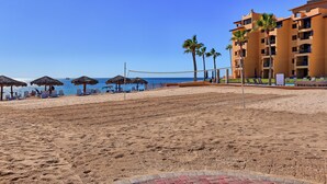 Una playa con sombrillas, sillas de descanso y un edificio con balcones.