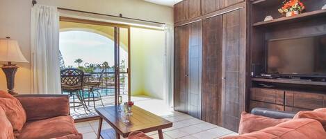 A living room with a TV, wooden cabinets, and a balcony with a pool view.