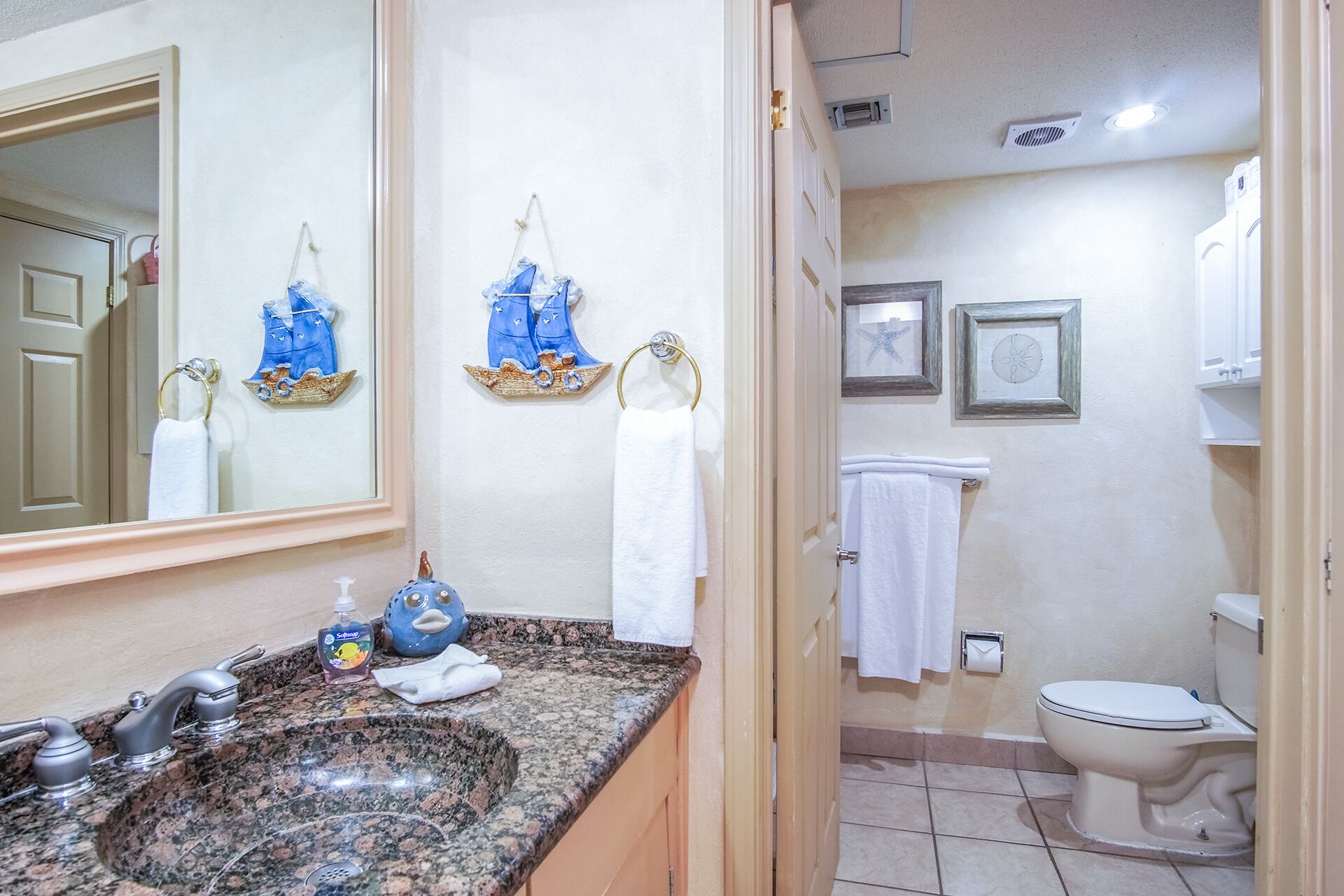 A bathroom with a granite sink, two towel rings, a toilet, and framed artwork on the wall.