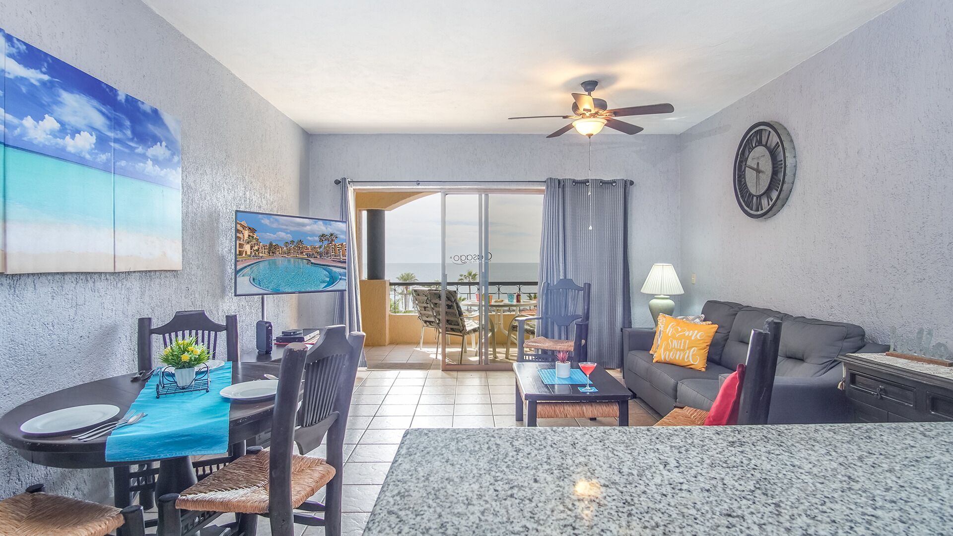 A modern living room with a dining area, a ceiling fan, a clock, and a view of the outdoors.