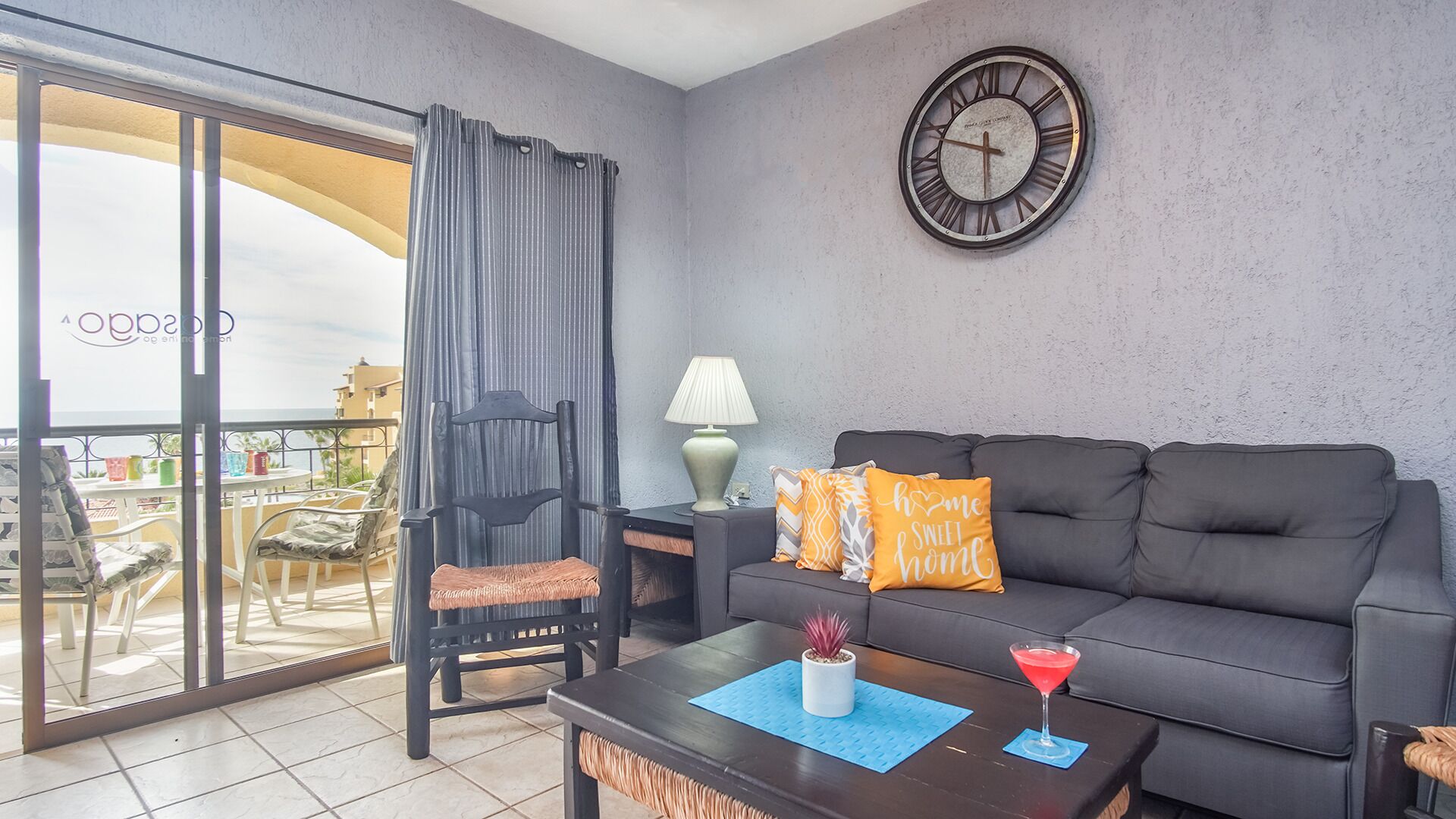A living room with a sofa, a chair, a table, a lamp, and a clock on the wall.