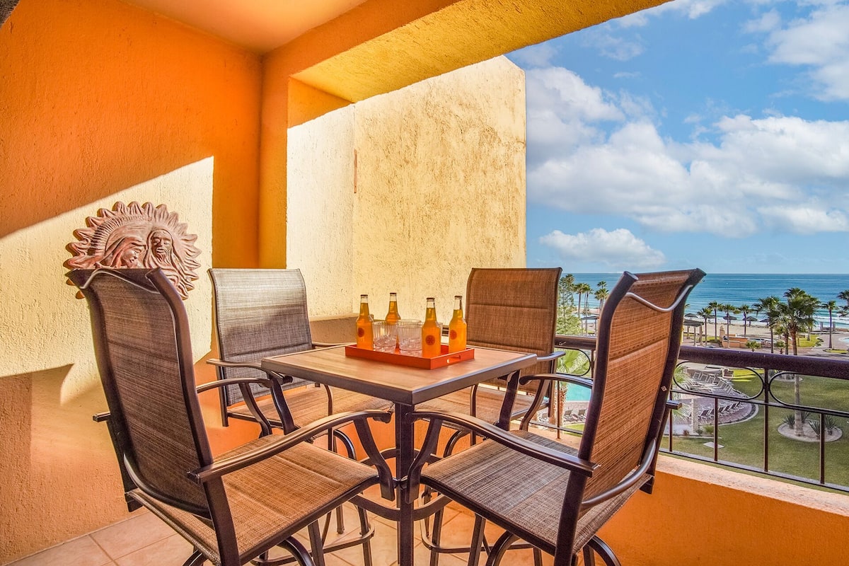 A balcony with a table set for two, featuring wicker chairs and a wooden table.