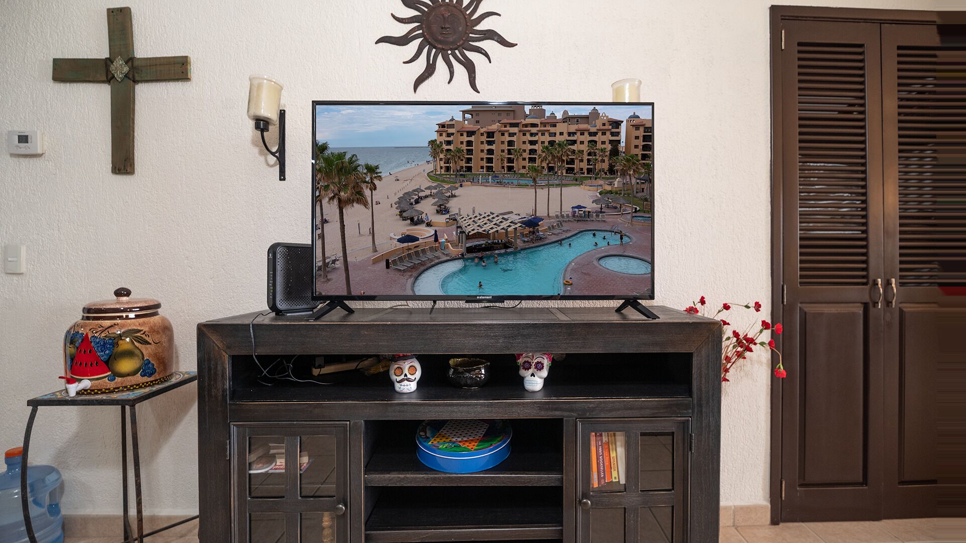 Ein Fernseher auf einem Holzboden mit Bild eines Poolresorts, einem Kreuz und einer Sonnendekoration an der Wand.