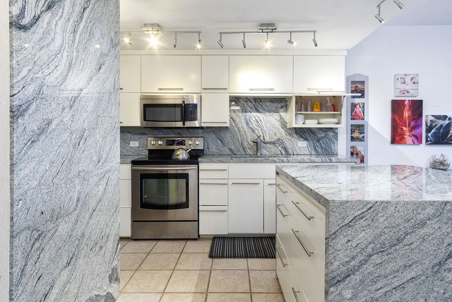 Una cocina moderna con armarios blancos, horno de acero inoxidable, microondas y encimera de granito.