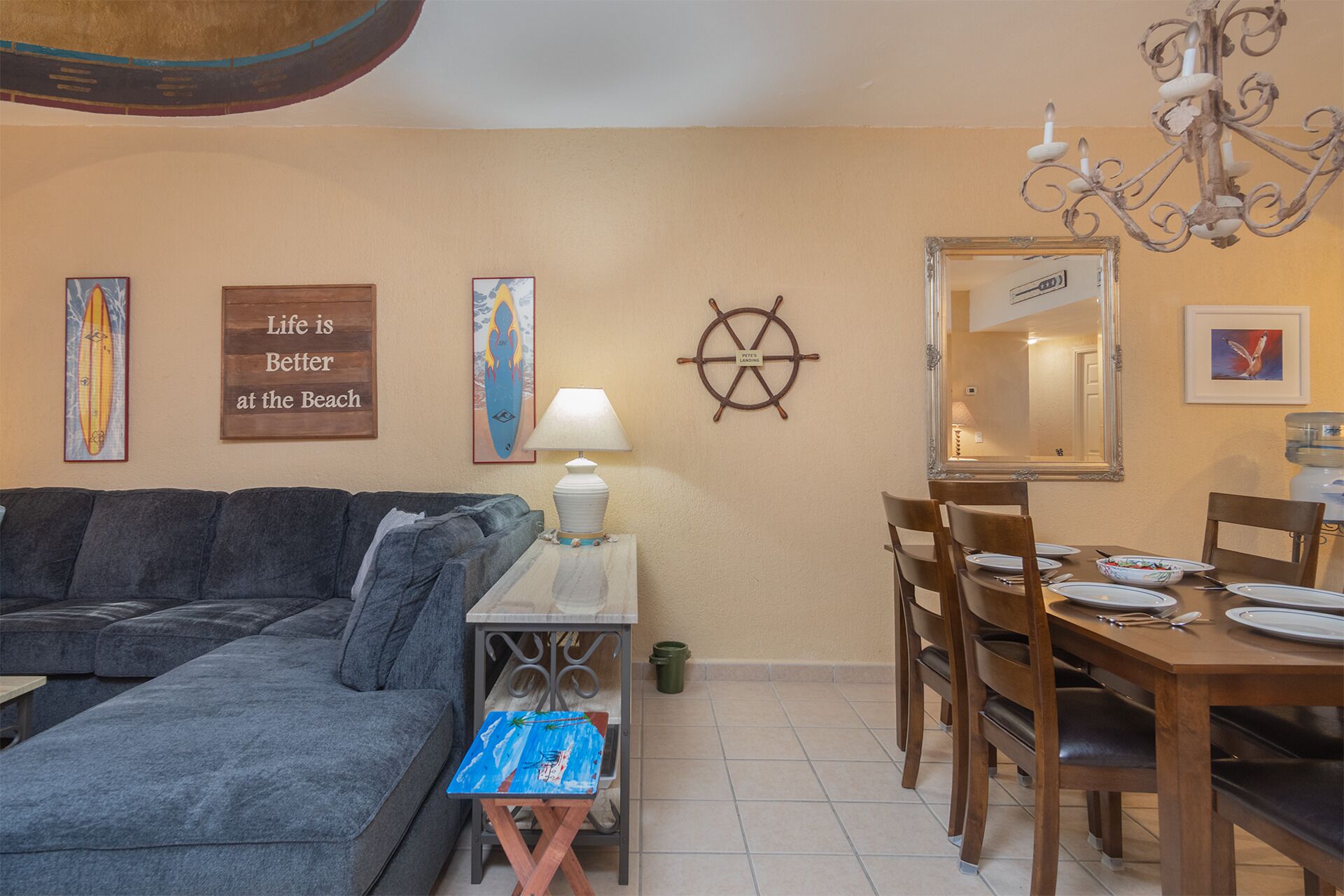 A living room with a gray sofa, a small table with a lamp, and a dining area with wooden chairs and a table set for four.