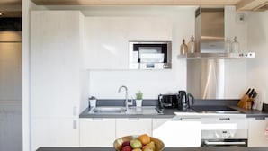 Une cuisine moderne avec des meubles blancs, un évier en acier inoxydable, un four encastré et une machine à café.