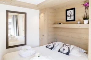 Ein Hotelzimmer mit Holzvertäfelung, einem Bett mit weißen Leinentüchern, einem großen Spiegel, einem gerahmten Bild an der Wand und einer Topfpflanze.