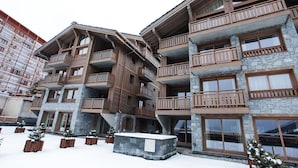 Un hôtel à plusieurs étages, doté de balcons, d’une façade en pierre et d’un terrain enneigé.
