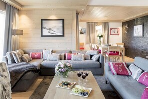 A cozy living room with a grey sofa, a coffee table with food and drinks, and a dining area with a table and chairs.