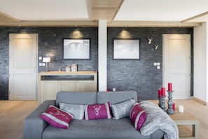 A modern living room with a grey sofa, decorative pillows, a wooden coffee table, and a stone wall backdrop.