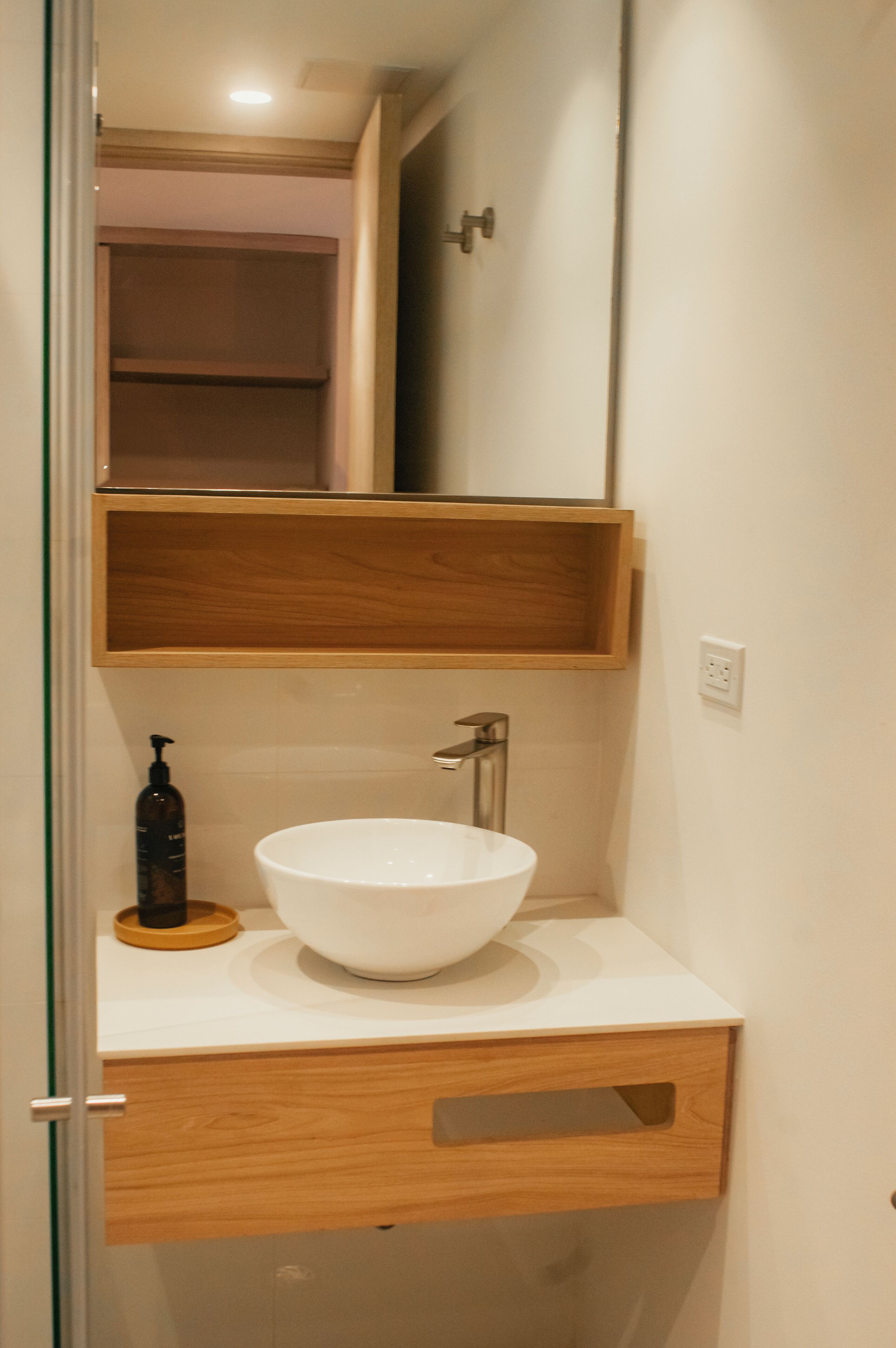 A bathroom with a white sink, wooden vanity, and a mirror above the sink.