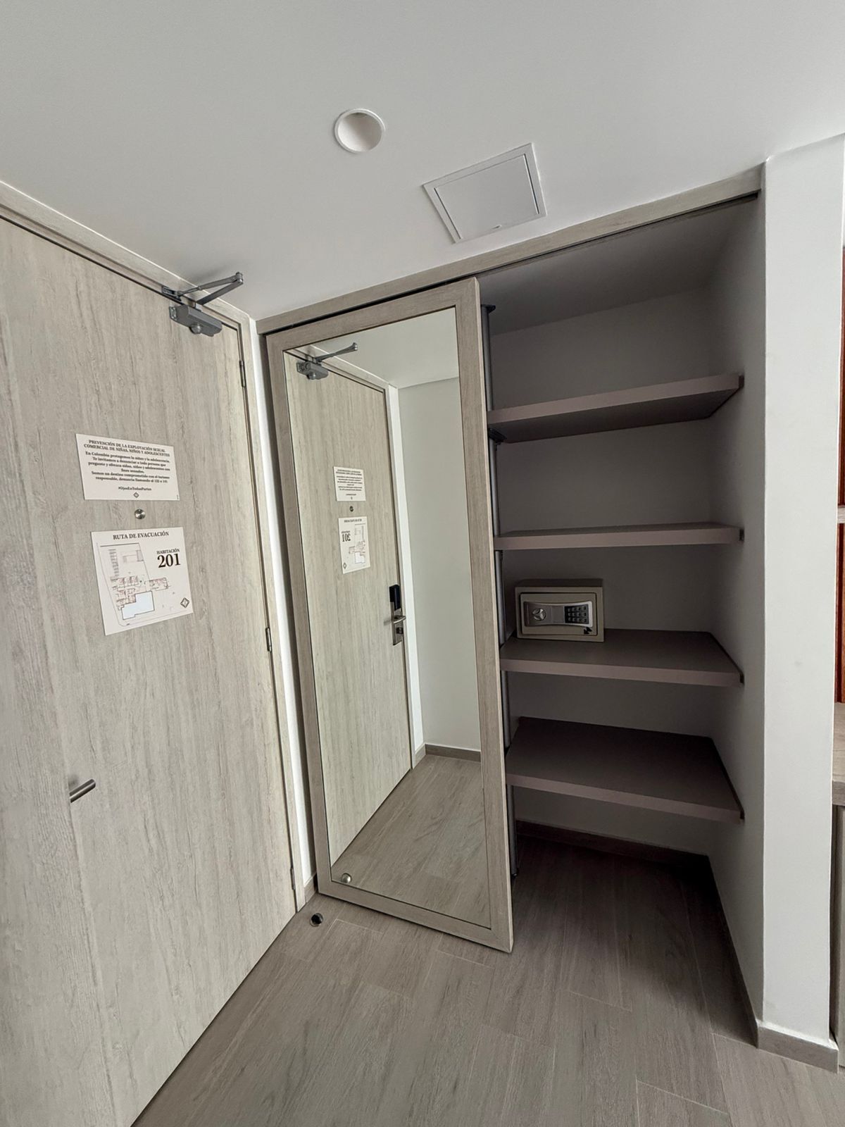 A room with a wooden door, a small safe, and a set of grey shelves.