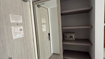 A room with a wooden door, a small safe, and a set of grey shelves.