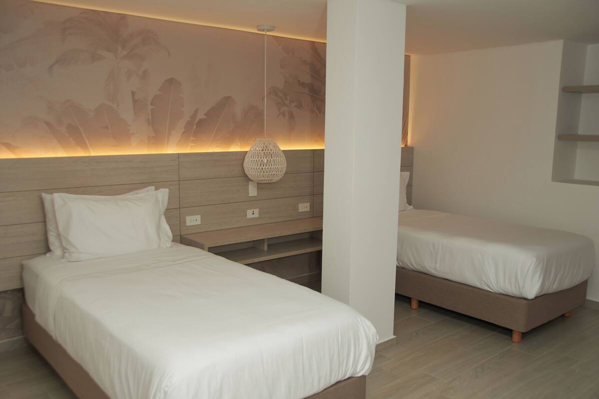 Una habitación de hotel moderna con dos camas individuales, un cabecero de madera, una lámpara de pared y una pequeña estantería.
