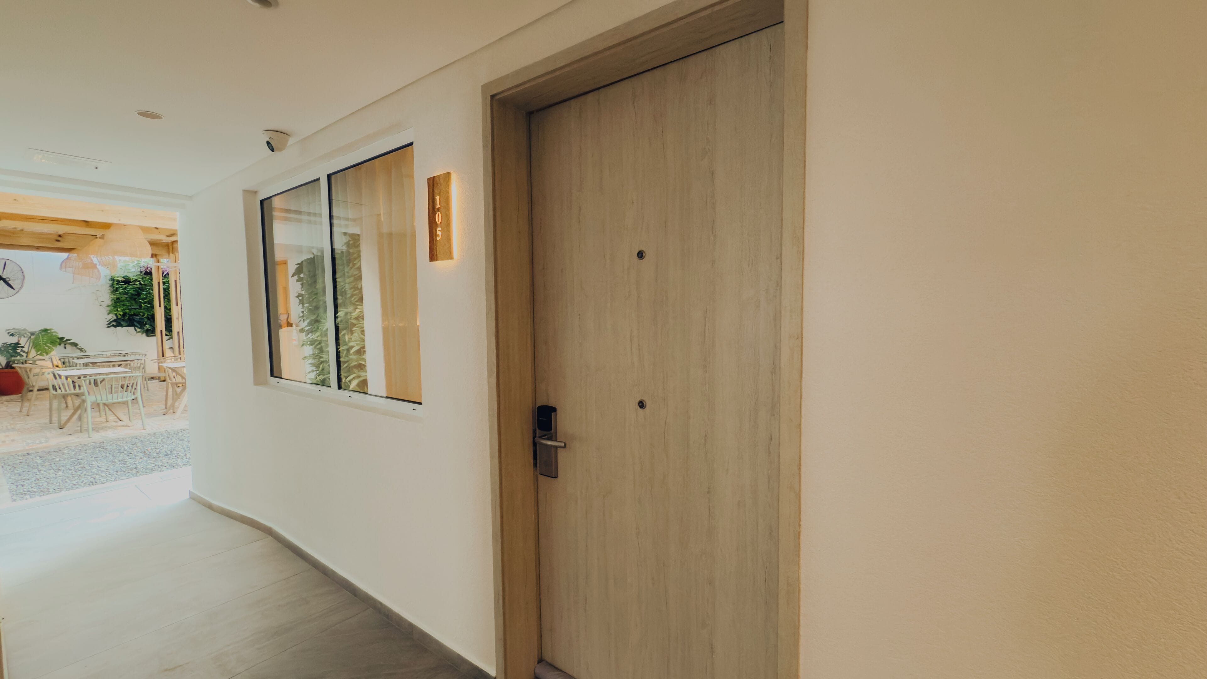 Un pasillo con una puerta de madera, una ventana que da a plantas de interior y un timbre.