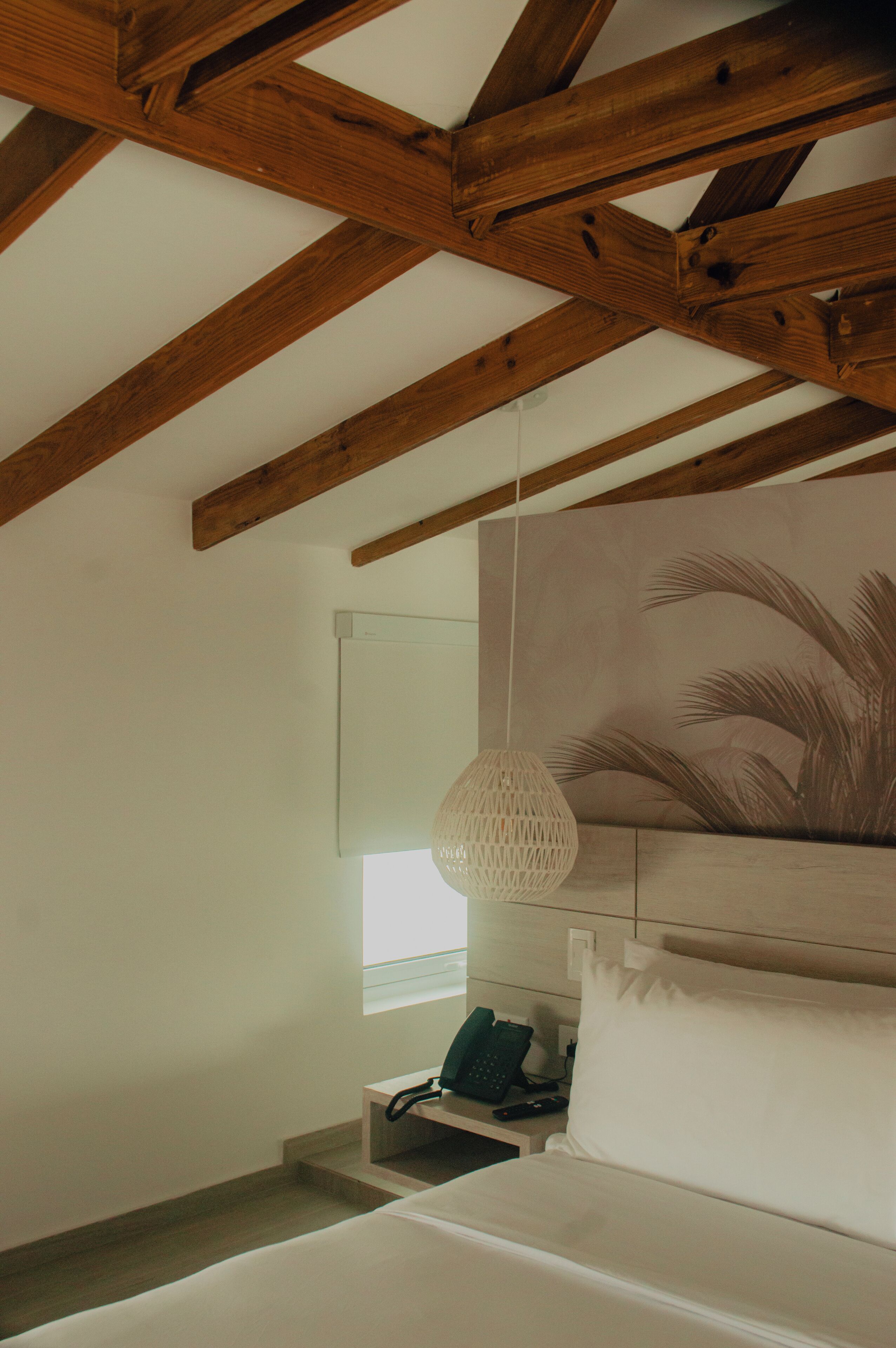 Un dormitorio con techo de madera, una cama, una mesita de noche, un teléfono y una lámpara de pared.