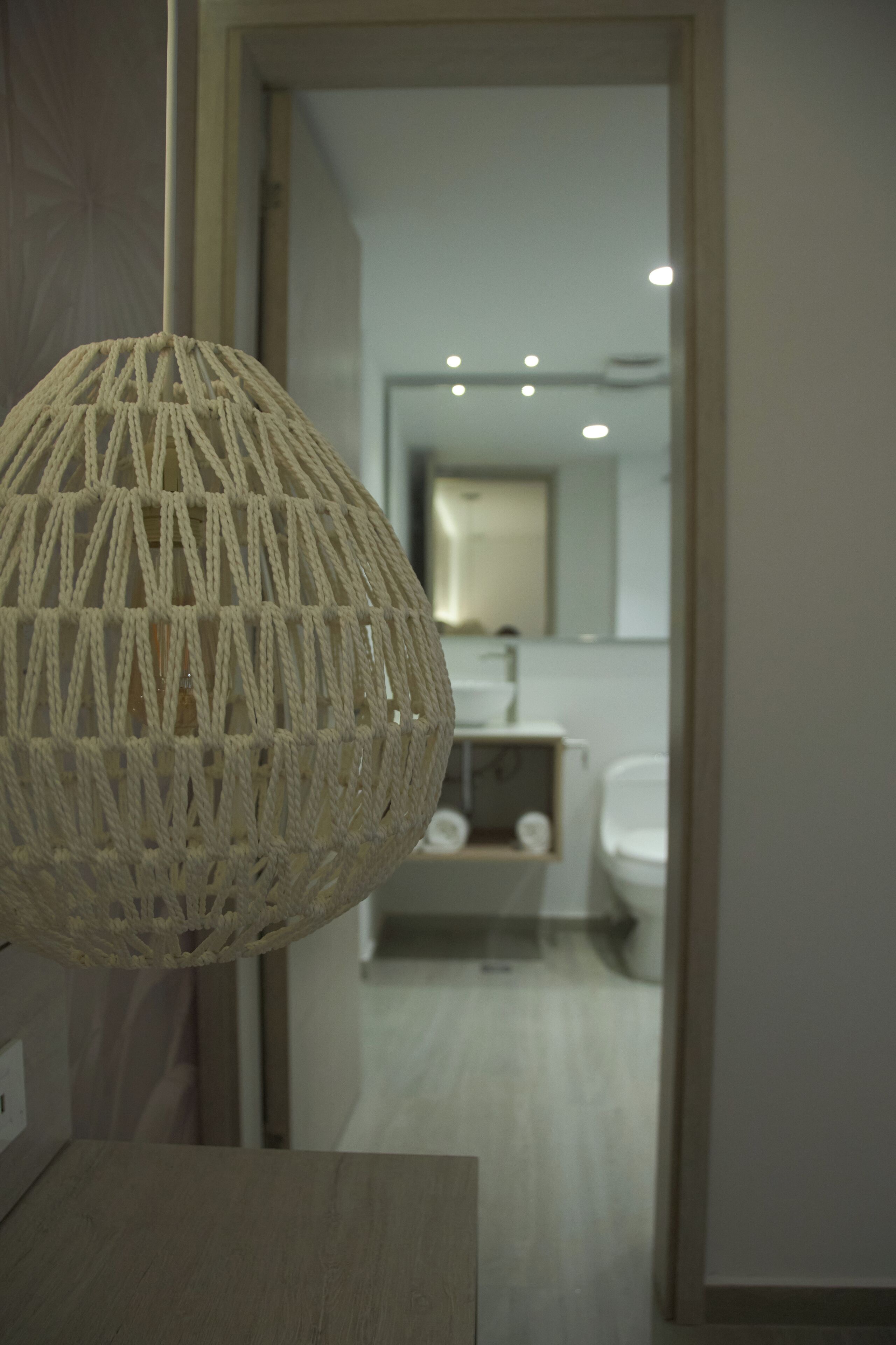 Luminária de macramê pendente em um banheiro moderno, com pia e espelho visíveis.