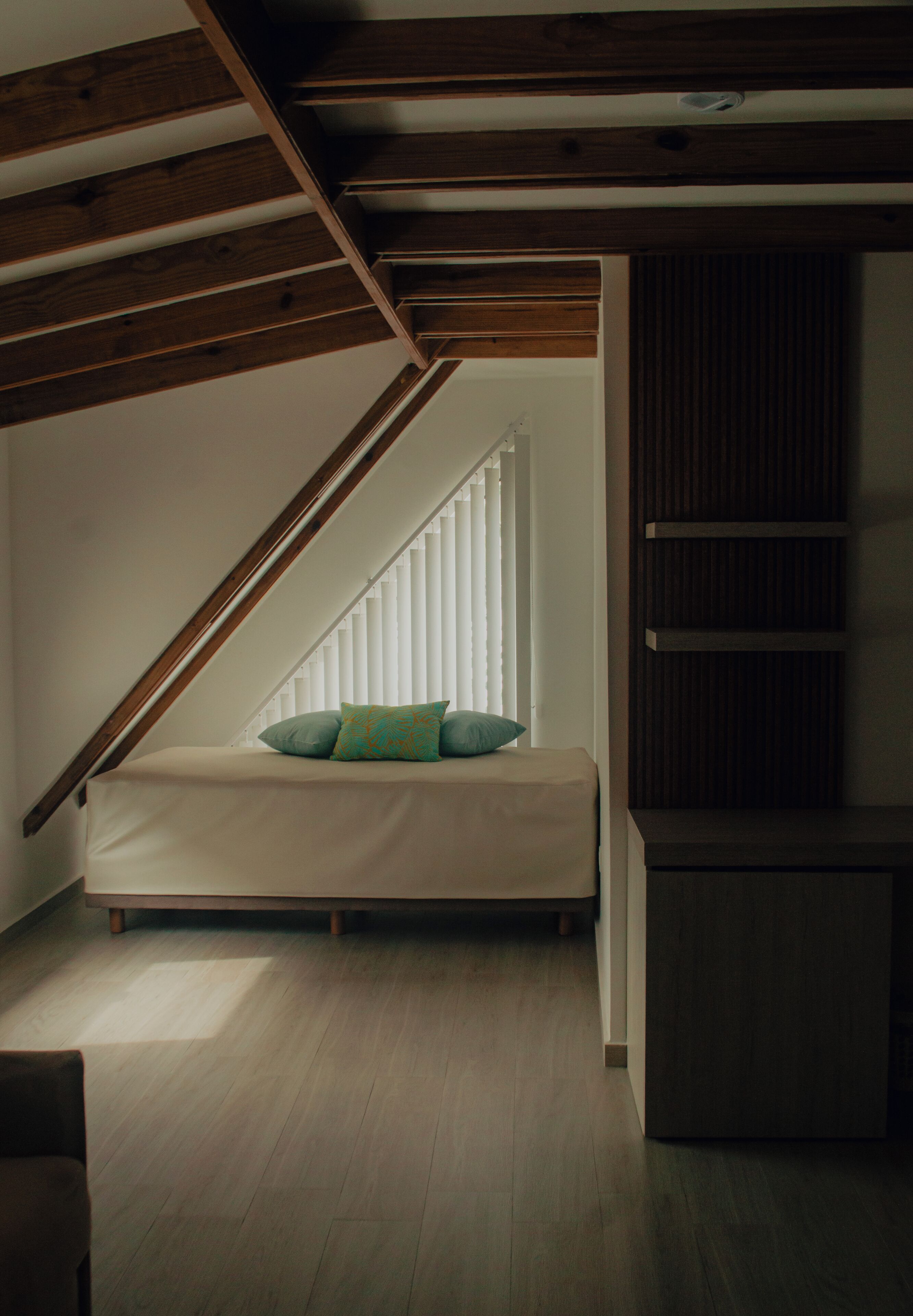 A loft bedroom with a sloped ceiling, a built-in bench with cushions, a wooden floor, and a built-in shelving unit.