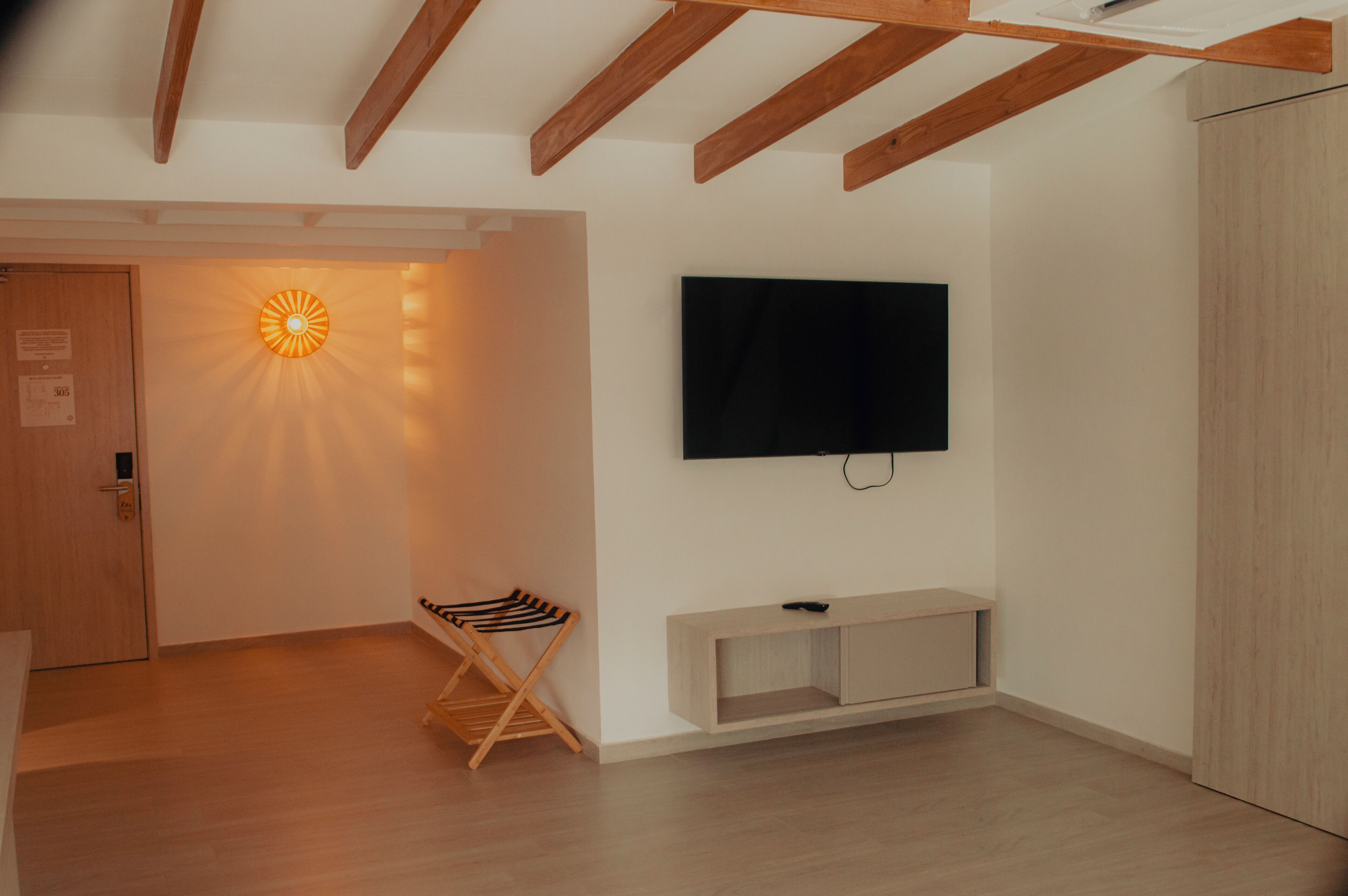 A modern living room with a wooden ceiling, a flat-screen TV mounted on the wall, a wooden bench, and a unique wall-mounted light fixture.