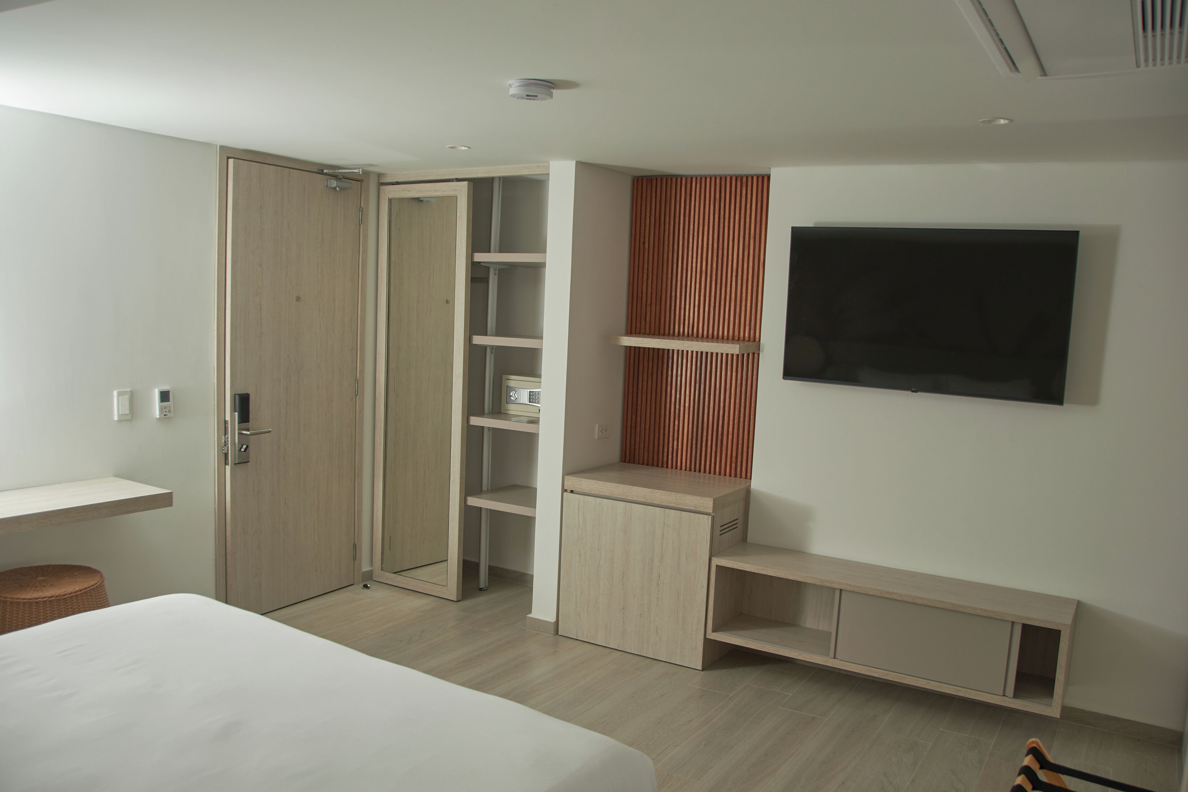 A modern bedroom with a bed, built-in wardrobe, shelving, and a TV mounted on the wall.