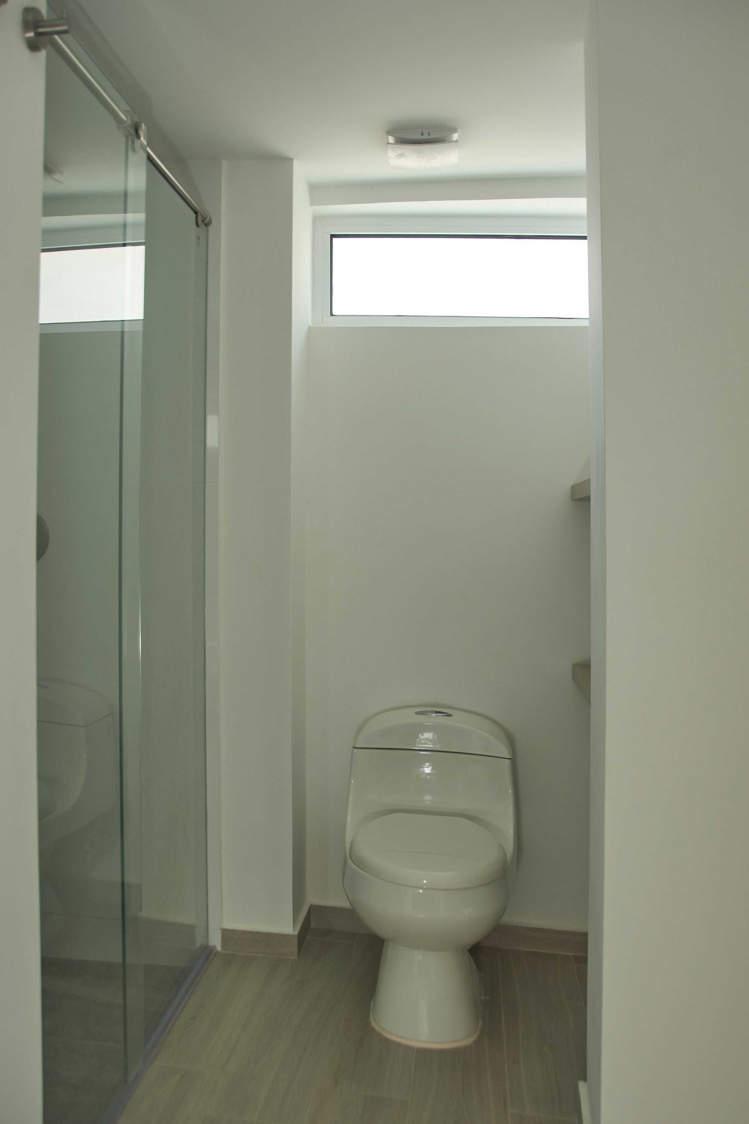Un baño pequeño y moderno con cabina de ducha de vidrio, inodoro y ventana que proporciona luz natural.