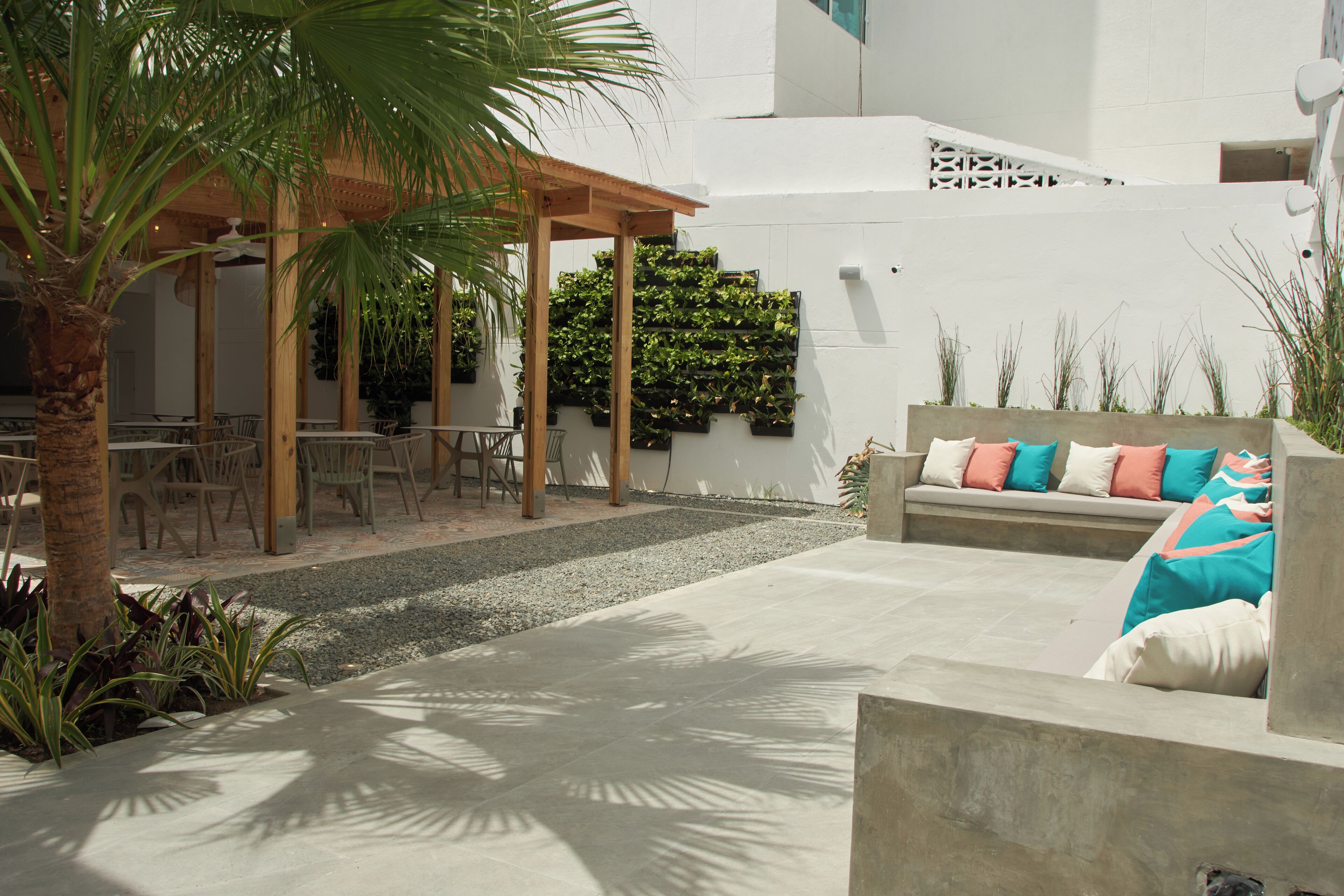 Ein Patio mit Holz-Pergola, Sitzgelegenheiten im Freien und einem an der Wand befestigten Pflanzgefäß mit Grünpflanzen.