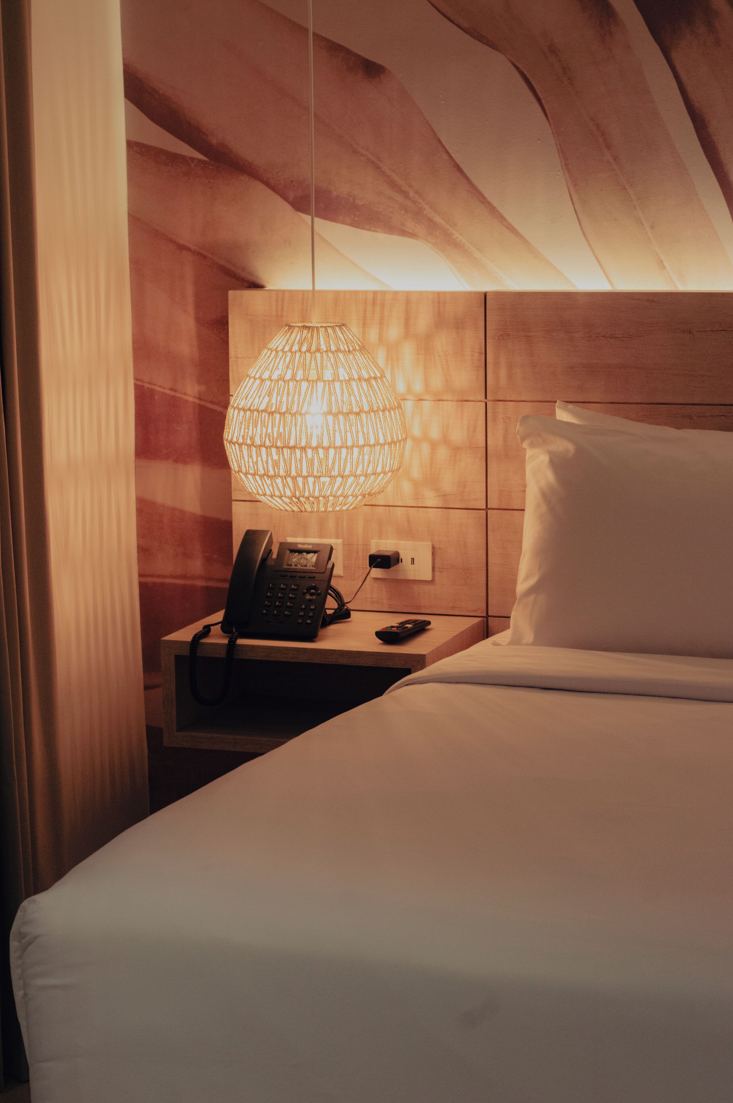 Una habitación de hotel con una cama, una mesita de noche con teléfono, una lámpara y una pared de madera.